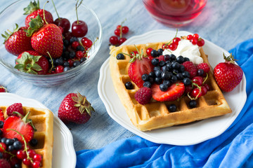 Healthy breakfast: Belgian waffles with sour cream, strawberry, raspberry, blueberry, cherry and red currant on blue wooden table. Selective focus