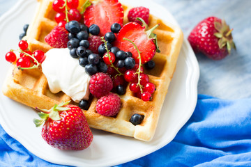 Healthy breakfast: Belgian waffles with sour cream, strawberry, raspberry, blueberry, cherry and red currant on blue wooden table. Selective focus