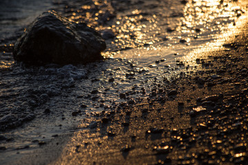 A close up of a shore at sunset, with light reflections on water and big and small stones