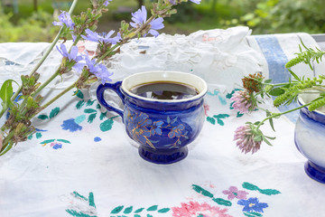Obraz na płótnie Canvas Blue cup of coffee tea chicory drink with chicory flower, hot beverage on embroidered fabric background