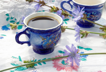 Blue cup of coffee tea chicory drink with chicory flower,  hot beverage on embroidered fabric background