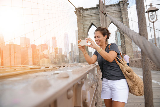 Tourist on Brooklyn bridge taking pictures with smartphone