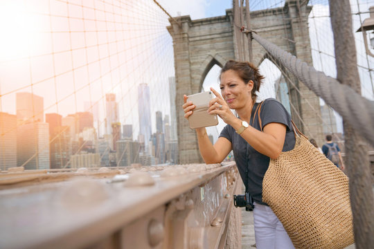 Tourist on Brooklyn bridge taking pictures with smartphone