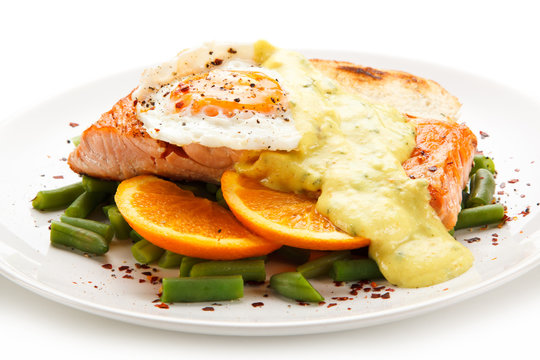 Grilled salmon with sauce, fried egg and vegetables on white background 