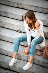 Modern woman sitting on stone steps, with healthy snack, cup str