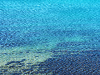 Turquoise blue background of an ocean space, view from above. Wavy sea surface. Kind of algae under water