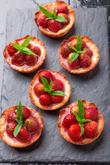 Naklejka premium Homemade strawberries tarts on slate plate, black background. Top view.