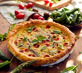 Vegetarian quiche with cherry tomatoes and green asparagus on a rustic wooden table