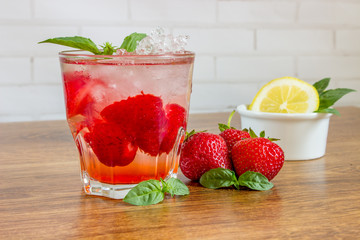 A refreshing summer drink with ice, strawberries and lemon on a wooden background. The concept of fruit drink.