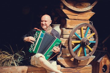 Mature man plays on a musical instrument accordion , is dressed in an embroidered shirt....