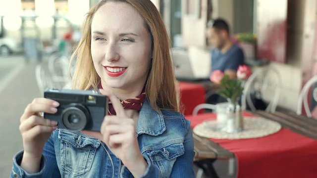 Pretty girl in denim jacket and with red lips doing photos on old camera, steadycam shot
