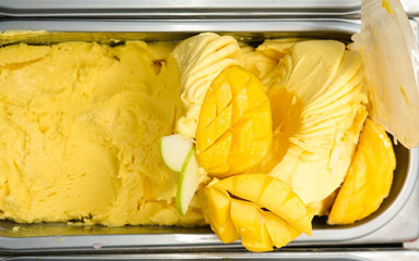 Mango Ice cream in ice cream tray, top view. selling ice cream concept with fresh mango fruit on...