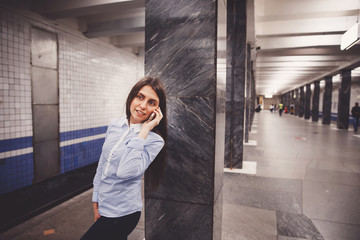 Young girl tourist talking on the phone in the subway and smiling. The concept is always in touch.