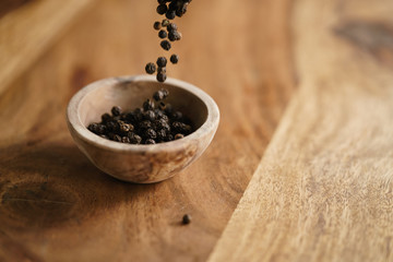 black dry pepper fall into wooden bowl on table