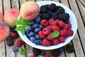 Raspberries, blue berries and black berries in a white bowl on a wooden garden table