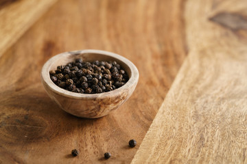 Fototapeta na wymiar black dry pepper in wooden bowl on table