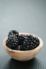 ripe organic blackberries in wood bowl on slate background