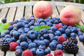 Peaches, raspberries, blue berries and black berries on a wooden garden table
