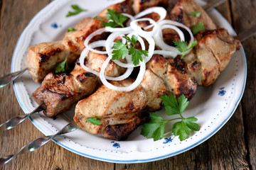 Home shish kebab from pork on skewers with pickled onion and parsley on an old wooden background.