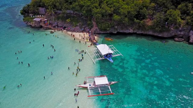 Aerial view flying over amazing of sandy beach with tourists swimming in beautiful clear sea water of the Sumilon island beach landing near Oslob, Cebu, Philippines.