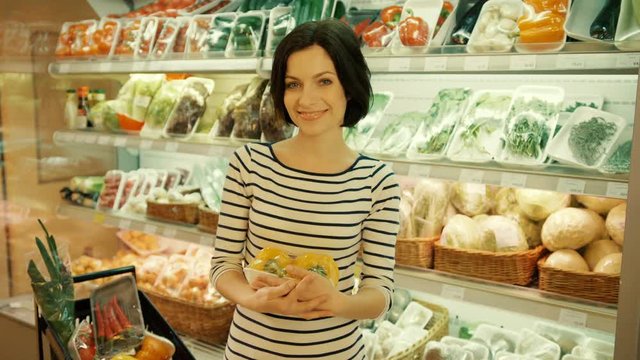 Portrait of young attractive woman, holding the papper and smiling on camera in the supermarket.
