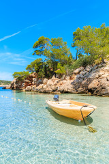 Yellow boat anchoring on idyllic Cala Portinatx beach and cliff rocks with pine trees in background, Ibiza island, Spain