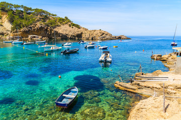 Fototapeta na wymiar Fishing and sailing boats on blue sea water in Cala Vadella bay, Ibiza island, Spain