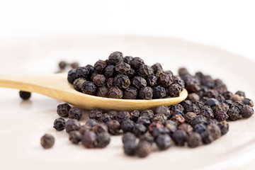 black peppercorns on wooden spoon.  closeup dried seeds.