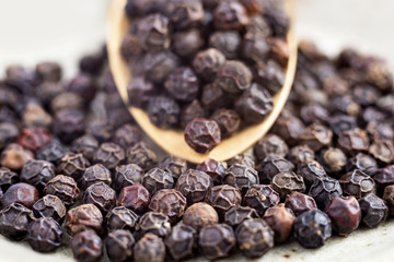 black peppercorns on wooden spoon.  closeup dried seeds.