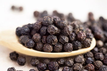Fototapeta na wymiar black peppercorns on wooden spoon. closeup dried seeds.