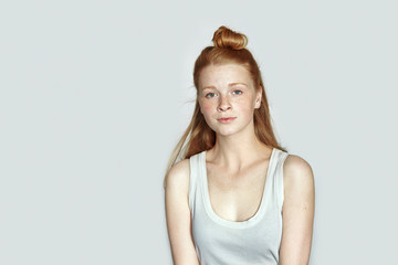 Close up portrait of young beautiful redhead beginner model woman in white t-shirt practicing posing showing emotions on white wall studio background with natural light