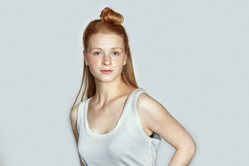 Close up portrait of young beautiful redhead beginner model woman in white t-shirt practicing posing showing emotions on white wall studio background with natural light