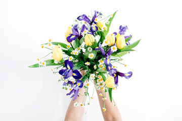 Girl's hands holding beautiful flowers bouquet: tulips, chamomiles, iris flower on white background. Flat lay, top view. Floral composition