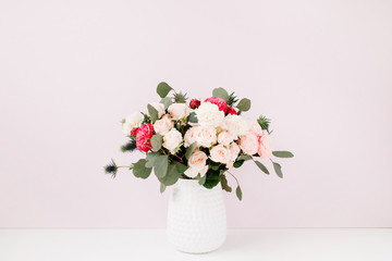 Beautiful flowers bouquet: bombastic roses, blue eringium, eucalyptus branches in flowerpot at pale pastel pink wall. Floral lifestyle composition.