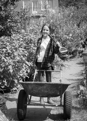 Black and white photo of teen girl posing with wheelbarrow at garden
