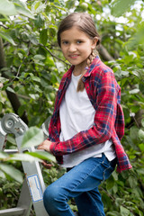 Smiling girl in red checkered shirt climbing up the stepladder at orchard