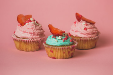 Closeup of three cupcakes with strawberry on pink background
