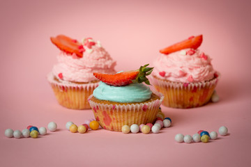 Three colorful cupcakes with strawberries on pink background with candies