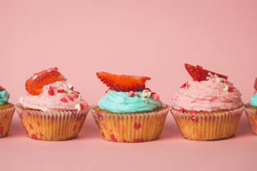 Closeup photo of colorful cupcakes with sprinkles and fresh strawberry in row
