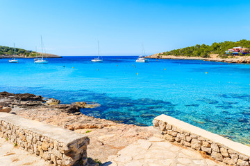 Fototapeta premium View of coastal promenade along blue sea in Cala Portinatx bay, Ibiza island, Spain