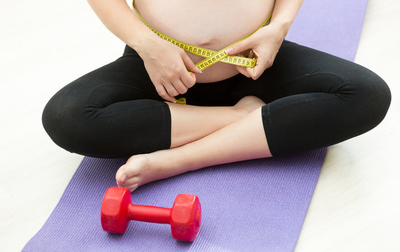 Pregnant woman measuring belly with tape after exercising on fitness mat
