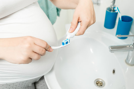 Closeup image of woman putting toothpaste on toothbrush at bathroom