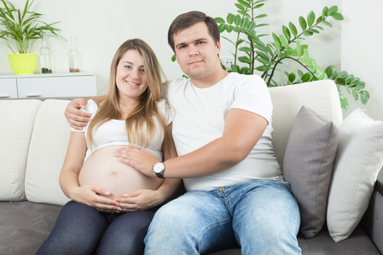 Portrait of happy pregnant couple sitting on sofa and looking at each other