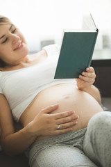 Portrait of young pregnant woman reading book on sofa