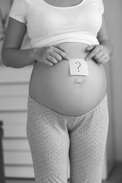 Black and white image of pregnant with question mark drawn on post-it sticker on belly