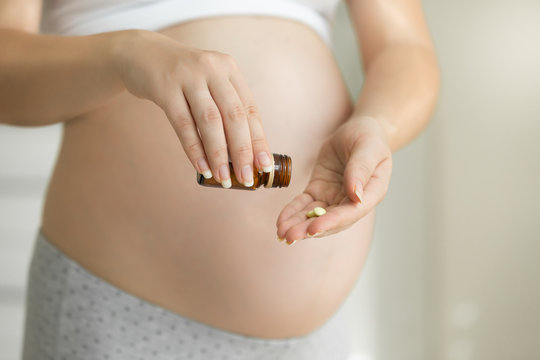 Closeup image of pregnant woman holding pills and medicine bottle