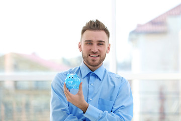 Happy young man holding piggy bank on blurred background