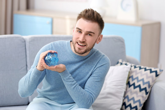 Happy young man holding piggy bank at home