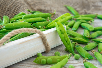 Pods of green peas outside in a small bowl on a wooden table