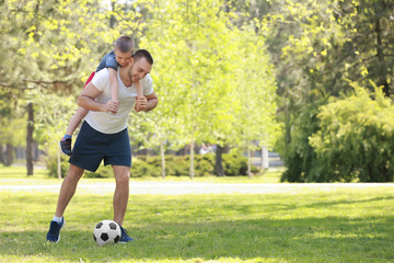 Father and son playing football on green grass in park